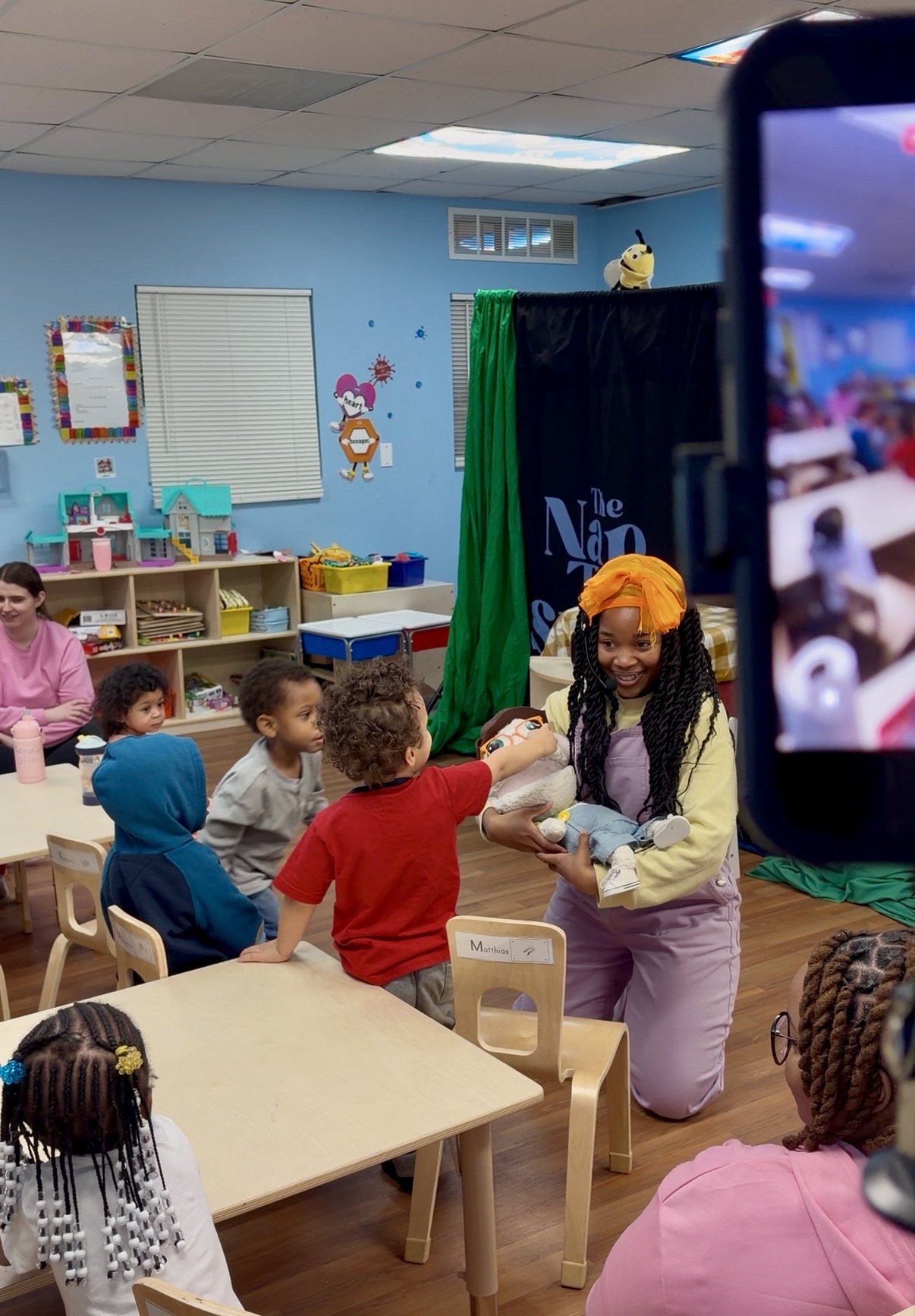 Performer kneeling to share a puppet with toddlers at a daycare table