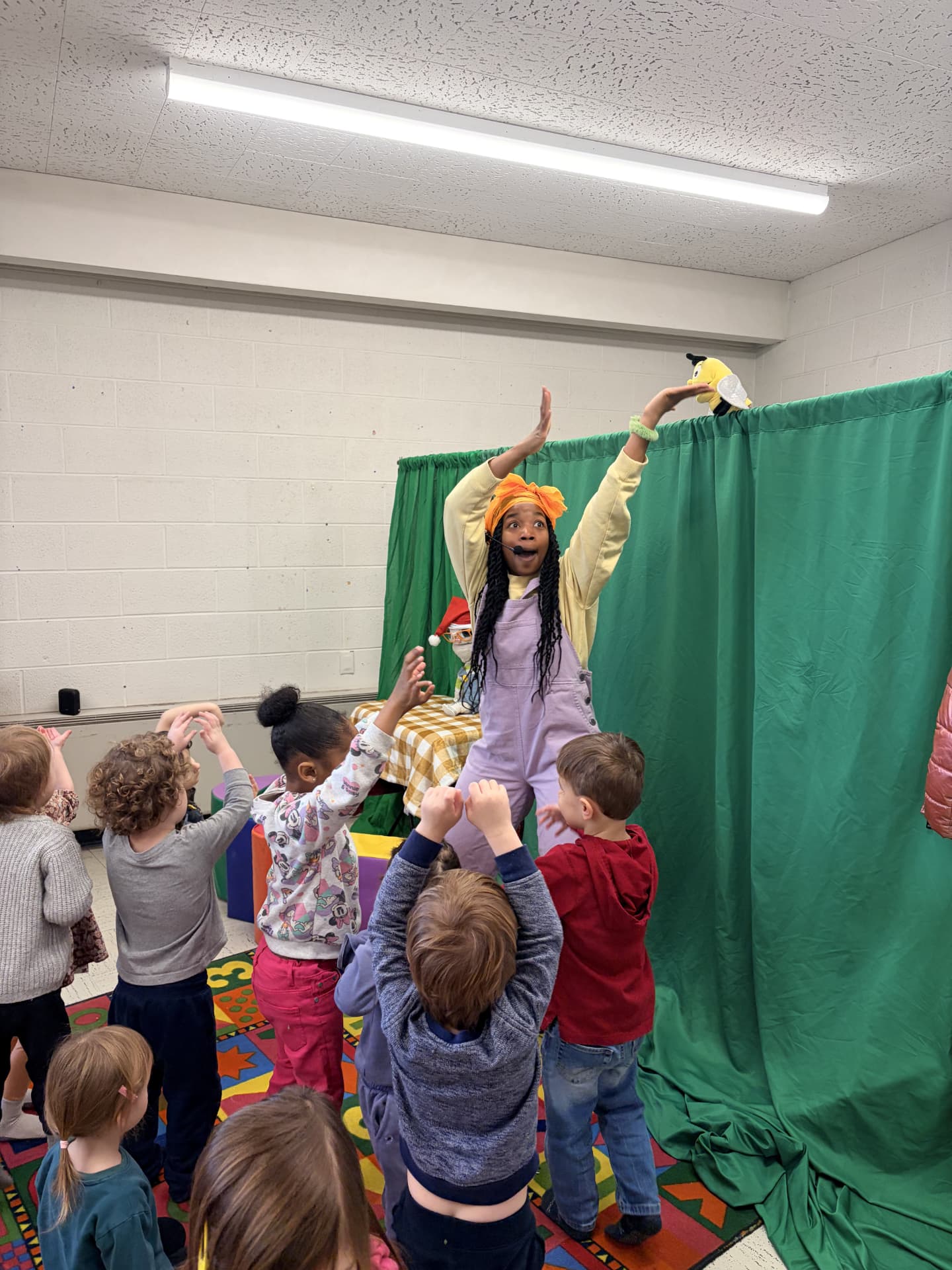 A Nap Time Show performer leading an interactive classroom moment with a puppet, surrounded by dancing children